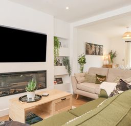 A living room with a wall-mounted television above a fireplace and green and beige sofas at Rydal Rock in Ambleside