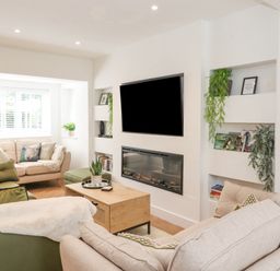 A living room with sofas a coffee table a wall-mounted television and built-in shelves with plants and books at Rydal Rock in Ambleside