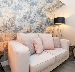 A living room with a two-seater sofa with cushions a floor lamp and a side table with a lamp at Fenty's in Bowness-On-Windermere