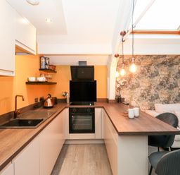 A kitchen with wooden countertops and black sink next to a lounge area with sofa and hanging lights at Fenty's in Bowness-On-Windermere