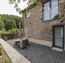 An outdoor seating area with a stone wall and patio furniture next to a stone house at Bank Hurst Coach House in Ulverston