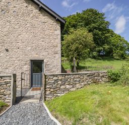 Stone house wall with a door and a small gate leading to a gravel path in a garden at Bank Hurst Coach House in Ulverston