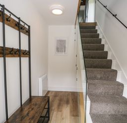 A hallway with a carpeted staircase and wooden bench with coat hooks at Bank Hurst Coach House in Ulverston