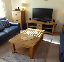 A living room with two dark blue sofas a wooden coffee table a TV on a wooden stand and wooden cabinets at House on the Green in Chipping Norton