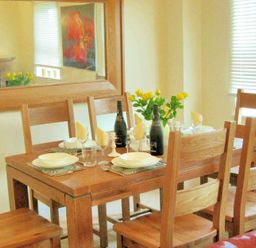 A dining table set with plates glasses napkins and bottles surrounded by wooden chairs at House on the Green Chipping Norton