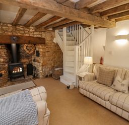 A living room with a stone fireplace a wood stove two sofas a white staircase and a lamp at Chippy Cottage in Chipping Norton