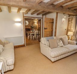 A living room with two striped sofas wooden beams and a lamp at Chippy Cottage in Chipping Norton