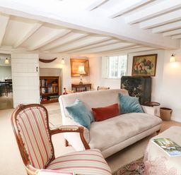 A living room with a sofa with cushions an armchair and a coffee table with books and magazines at Holly Cottage in Minster Lovell