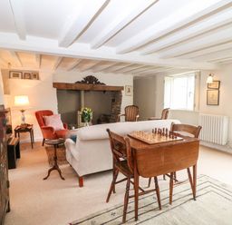 A living room with a wooden chess table and chairs a sofa armchairs and a fireplace at Holly Cottage in Minster Lovell