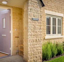 An open front door showing part of a stone house with a window and plants at The Bybrook in Bourton-on-the-Water
