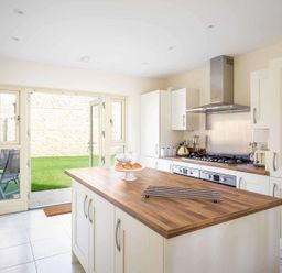 A kitchen with an island wooden countertop and open doors leading to a garden at The Bybrook in Bourton-on-the-Water