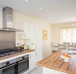 A kitchen with two ovens a gas stove a toaster and a dining table with chairs at The Bybrook in Bourton-on-the-Water