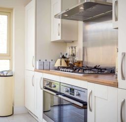 A kitchen with white cabinets a wooden countertop a gas stove double oven and a beige trash can at The Bybrook in Bourton-on-the-Water