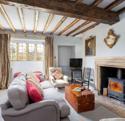 A living room with a sofa and armchair facing a wood burning stove with a wooden coffee table and exposed wooden ceiling beams at Shenley Broadwell