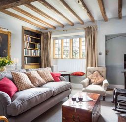 A living room with a gray sofa with cushions a wooden chest a rocking chair and a window seat at Shenley Broadwell