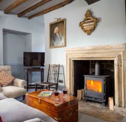 A living room with a wood burning stove in a stone fireplace wooden chest as coffee table sofa armchair and TV at Shenley in Broadwell