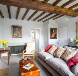 A living room with a gray sofa with cushions a wooden chair a wooden coffee table with two glasses and a magazine a side table with yellow flowers and framed portraits on the walls at Shenley in Broadwell