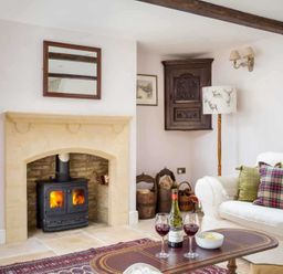 A living room with a fireplace wood burning stove sofa table with wine and glasses at Oyster Barn in Naunton