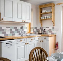 A kitchen with white cabinets a wooden countertop a stainless steel sink a kettle and cups on a wooden shelf at Oyster Barn in Naunton