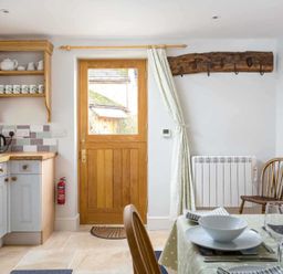 A kitchen with wooden door and shelf with mugs next to a dining table set with plates glasses and cutlery at Oyster Barn in Naunton
