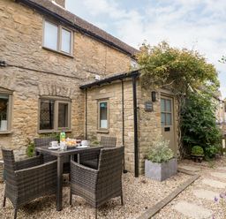 An outdoor stone patio with a table set for breakfast and four wicker chairs at Spinners Cottage in Stow-on-the-Wold