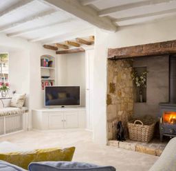 A living room with a wood burning stove books a TV and a window seat at Stanley Cottage in Chipping Campden