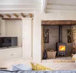 A living room with a wood burning stove fireplace a television and built in shelves at Stanley Cottage in Chipping Campden
