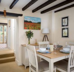 A dining room with a wooden table set for four and a sideboard with a lamp flowers and wall art at Lanes Cottage in Chipping Campden