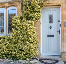 A light blue front door next to tall windows with climbing plants covering the stone wall at Green Pump Cottage in Blockley