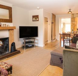 A living room with a fireplace a TV a dining table and sofas at Green Pump Cottage in Blockley