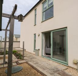 A backyard patio with sliding glass door wooden pergola and garden beds at Pebbles Reach in Fortuneswell