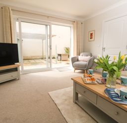 A living room with a television on a stand a coffee table with cups and flowers an armchair and a sofa near sliding glass doors at Pebbles Reach in Fortuneswell