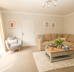 A living room with a beige sectional sofa a grey armchair a wooden coffee table with snacks and flowers at Pebbles Reach in Fortuneswell