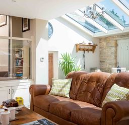 A living area with a brown leather sofa and green patterned cushions natural light from a glass ceiling wooden table with cups and snacks East Leaze Chipping Campden