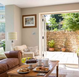 A living room with leather sofas a wooden coffee table with cups and pastries and an open door leading to a stone patio at East Leaze in Chipping Campden