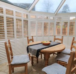 A dining area with a round wooden table and six wooden chairs with cushions in a conservatory at East Leaze in Chipping Campden