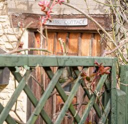 A wooden door behind a green lattice fence with plants and a stone wall at Carters Cottage in Stow on the Wold