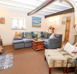 A living room with a sectional sofa a striped armchair and ottoman a wooden chest coffee table and paintings on the wall at Carters Cottage in Stow-on-the-Wold