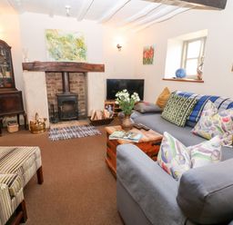 A living room with a fireplace a sofa with cushions a wooden coffee table and a TV at Carters Cottage in Stow-on-the-Wold