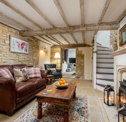 A living room with a brown leather sofa a wooden coffee table a patterned rug stone walls exposed wooden beams and a fireplace at Eastnor in Moreton-in-Marsh