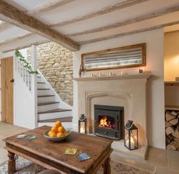 A living room with a wooden coffee table holding a bowl of oranges near a fireplace with candles and stacked firewood at Eastnor Moreton-in-Marsh
