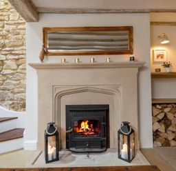 A fireplace with a fire burning two lanterns with candles and a mirror above it at Eastnor Moreton-in-Marsh