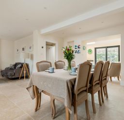 A dining area with a table and six chairs set with cups and plates next to a seating area with a sofa and coffee table at Wall Cottage in Burford