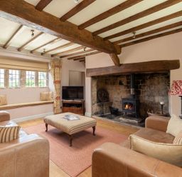 A living room with exposed wooden beams a wood stove leather sofas and a window seat at Little Gables in Broadway