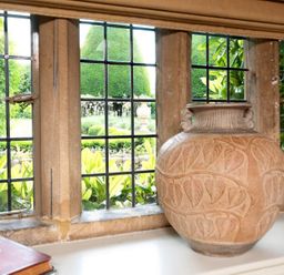 A large decorated ceramic vase on a window sill with a garden visible through black grid windows at Little Gables in Broadway