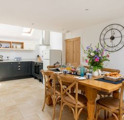 A kitchen with dark cabinets and a wooden dining table with chairs and flowers at Copperbeech in Stow-on-the-Wold