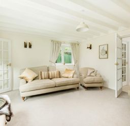 A living room with beige sofas cushions a window with curtains and open French doors at Holly Cottage Middle Tysoe in Tysoe