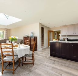 An open kitchen and dining area with a round table set for breakfast and wooden chairs in Mount View in Childswickham
