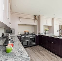 A kitchen with marble countertops dark lower cabinets beige upper cabinets stove and refrigerator at Mount View in Childswickham
