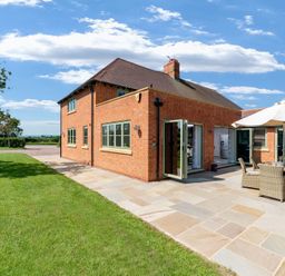 A brick house with several windows and a patio with outdoor furniture and an umbrella surrounded by a lawn at Mount View in Childswickham